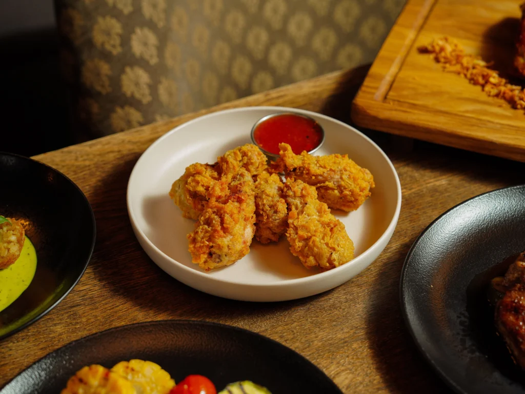 Plate of crispy fried chicken served with dipping sauce on a wooden table, perfect for food photography.
