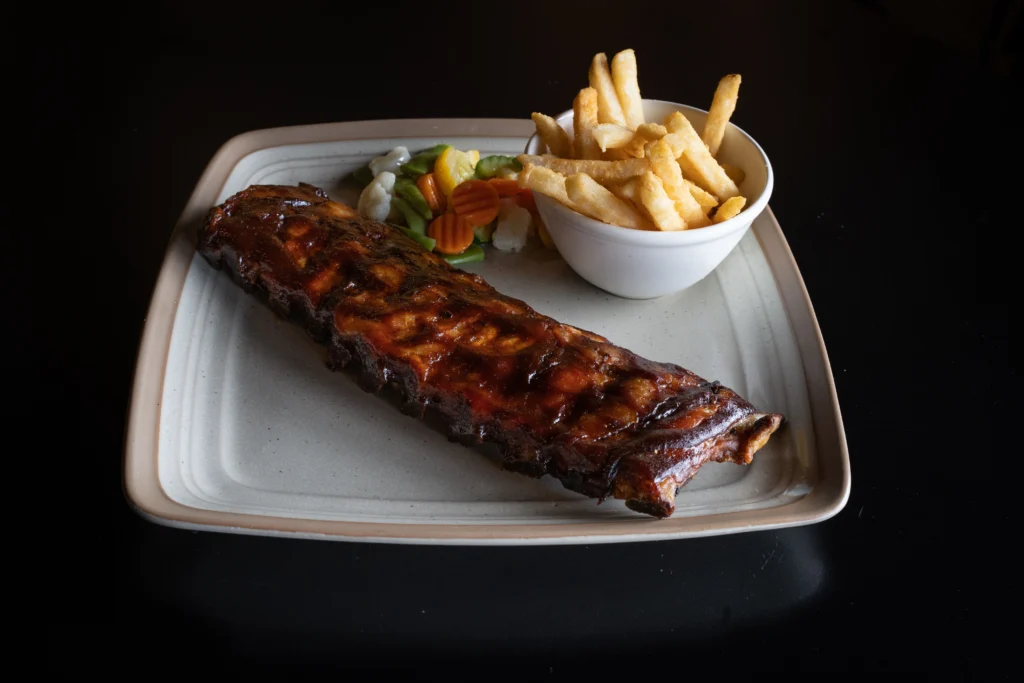 Delicious BBQ spare ribs served with french fries and mixed vegetables on a plate.